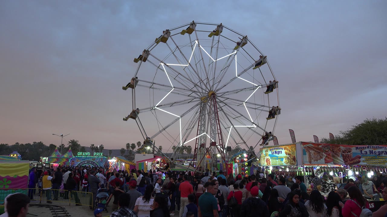 Neon Ferris wheel above a crowded fairground at dusk.