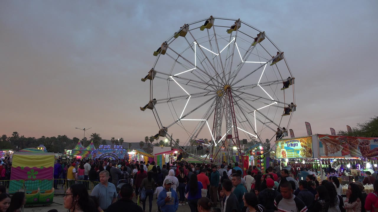 Large Ferris wheel with star lights above a packed fair walkway.