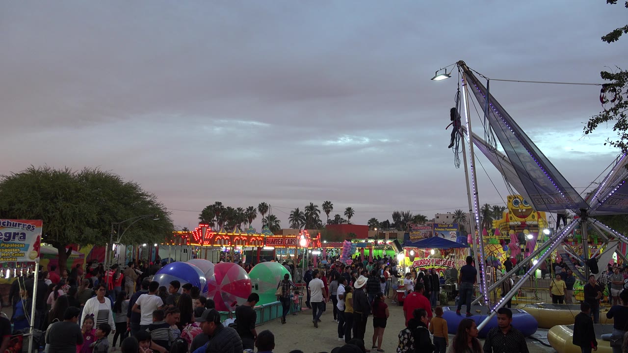 Crowded fairground with bungee tower and cloudy dusk sky.