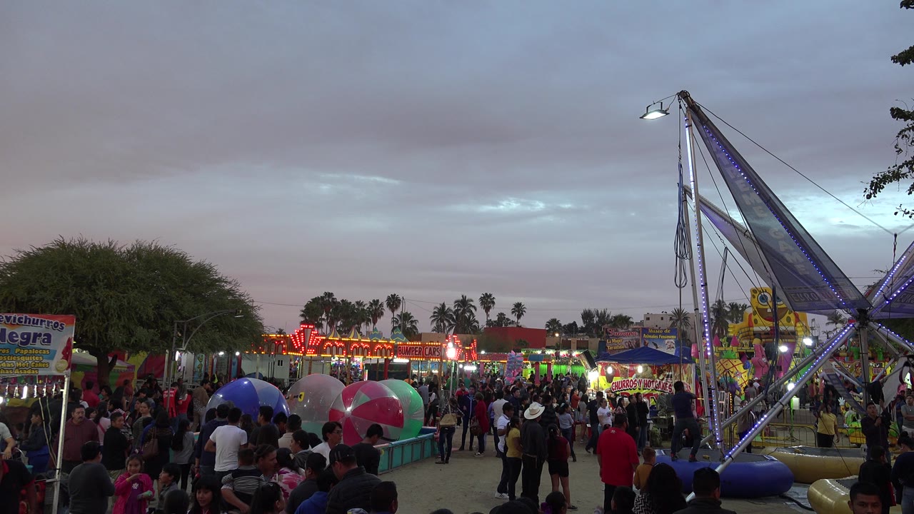 Crowded carnival midway at dusk with a tall ride frame on the right.