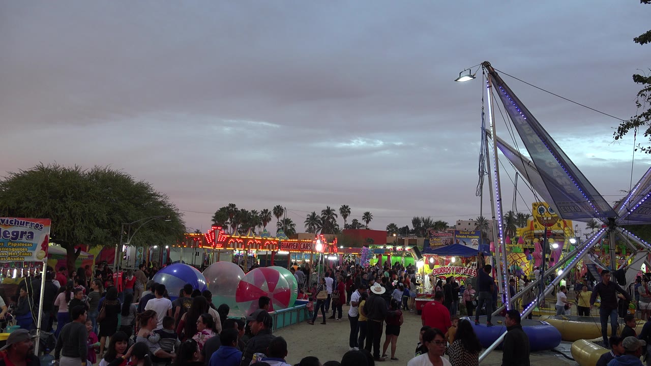 Crowded amusement park with ride lights and inflatable balls at dusk