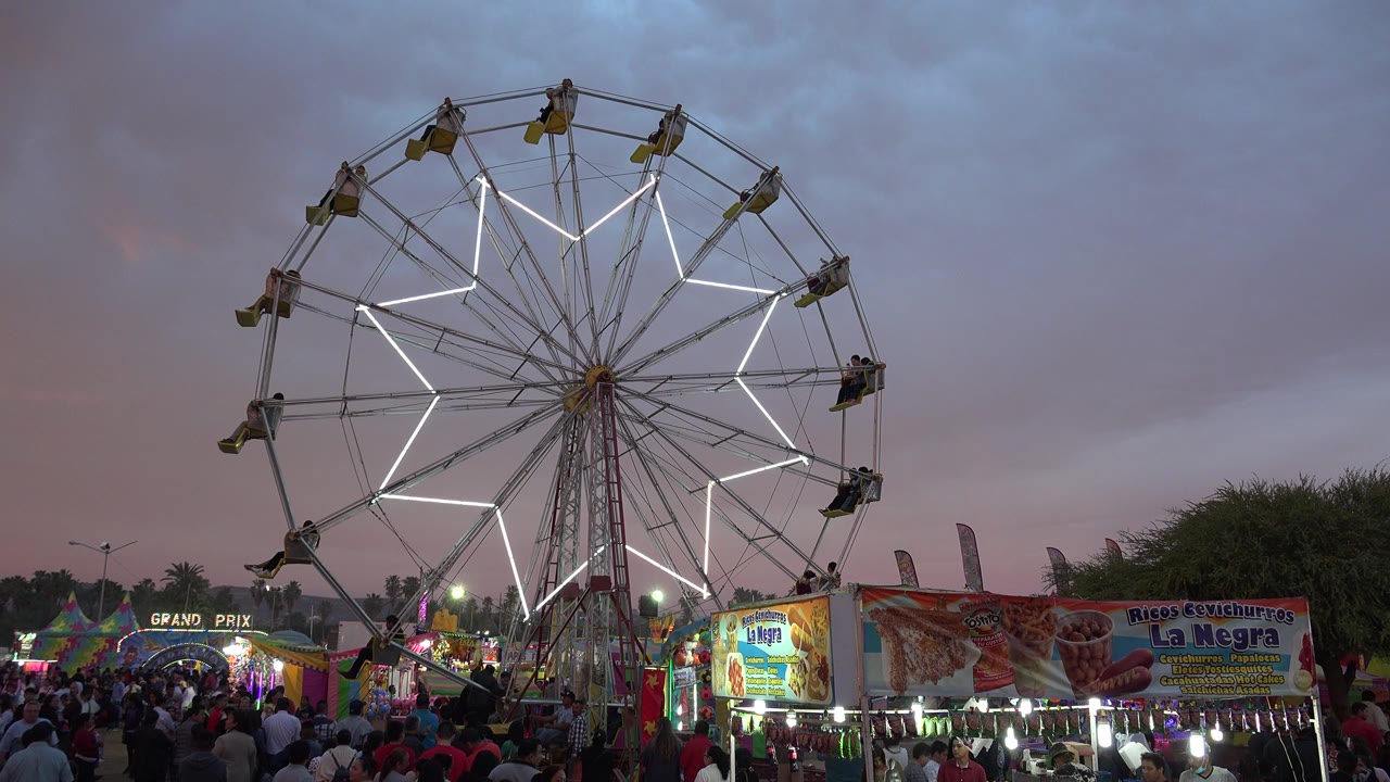 Ferris wheel with white lights above a crowded fairground.