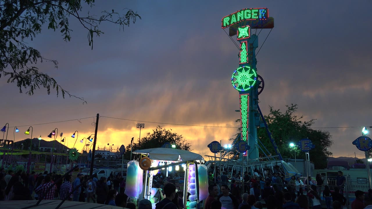 Illuminated Ranger fair ride at sunset under cloudy sky.