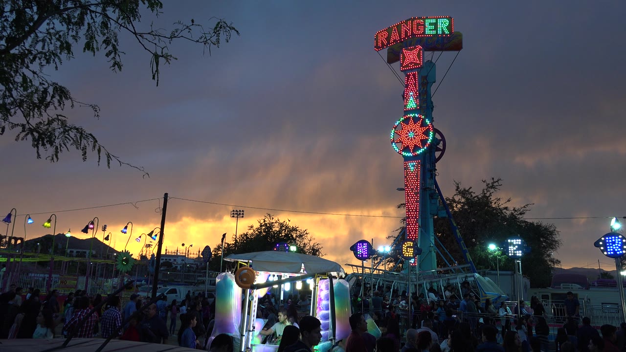 Illuminated Ranger ride above a crowded fair at sunset.