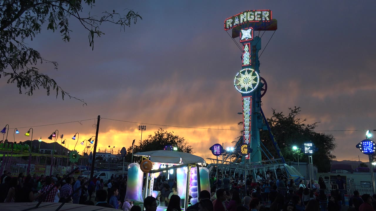 Tall illuminated fair ride over a crowd at dusk.