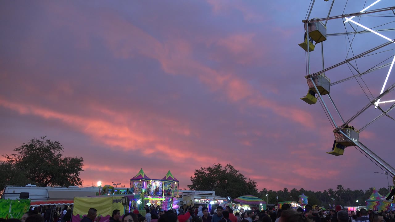 Ferris wheel edge over a crowded carnival at sunset.
