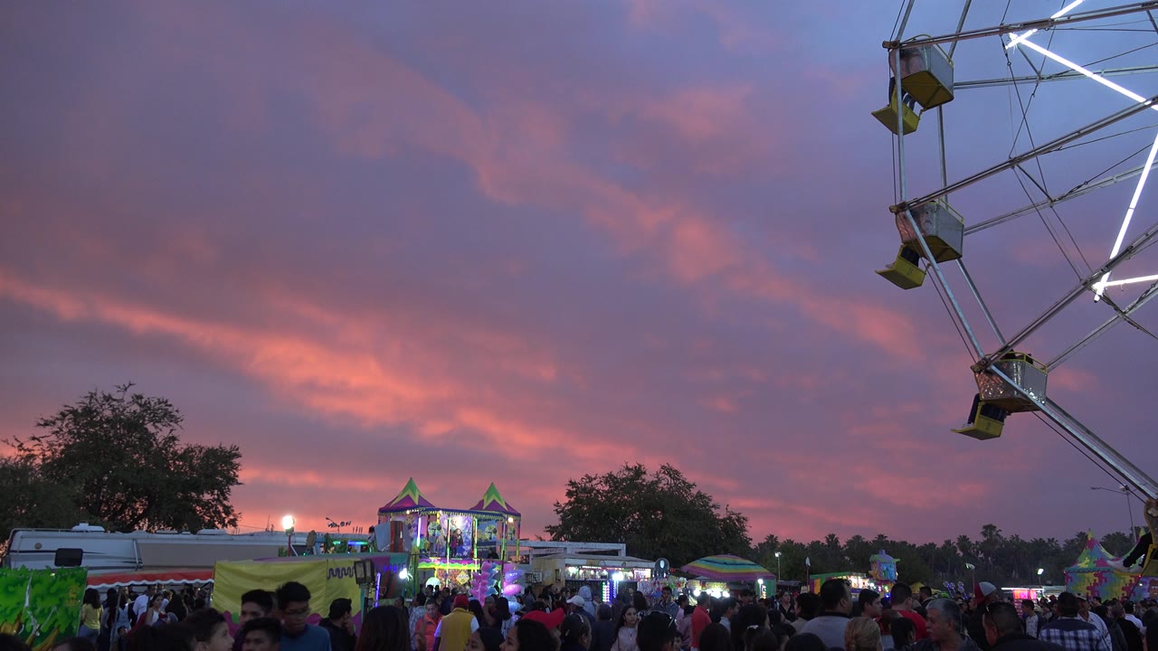 Crowded fairground with a Ferris wheel at dusk.