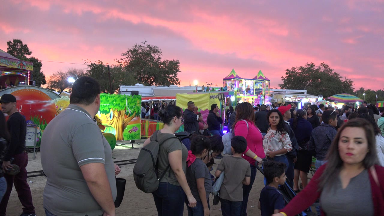 Crowd waiting near a carnival ride at sunset.