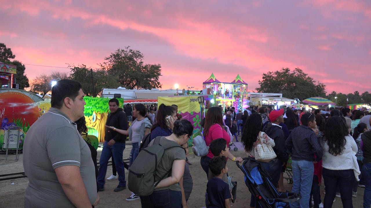 Crowd of parents and children waiting near a colorful amusement ride at sunset.