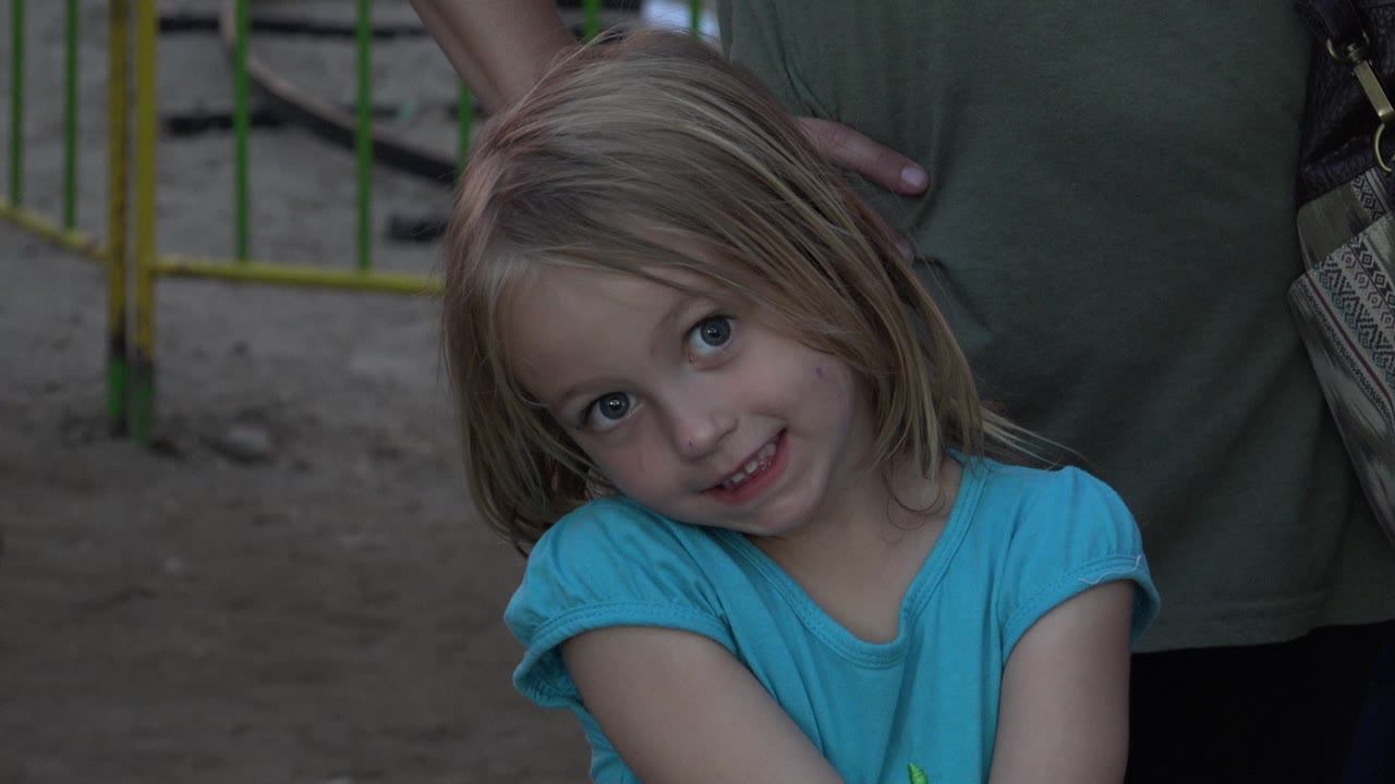 Blonde girl smiling with fencing visible behind her.