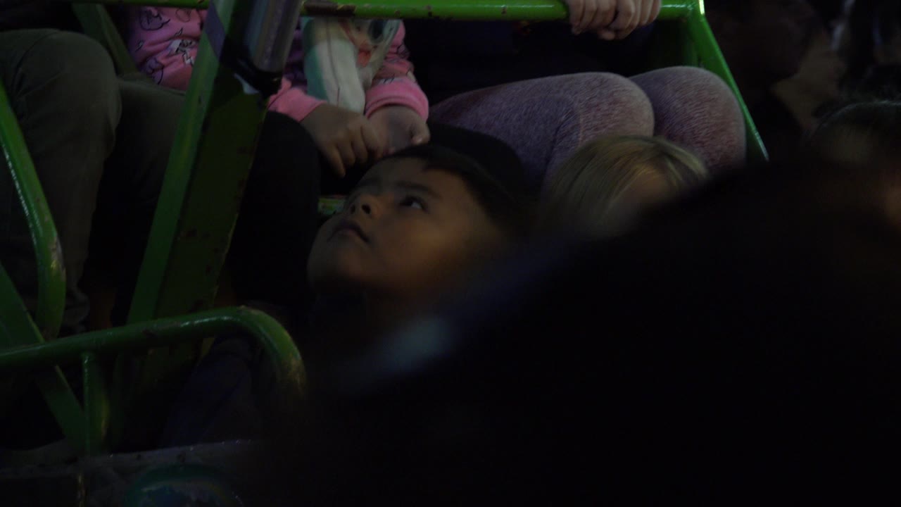 Children seated behind green metal rails in dim indoor light.