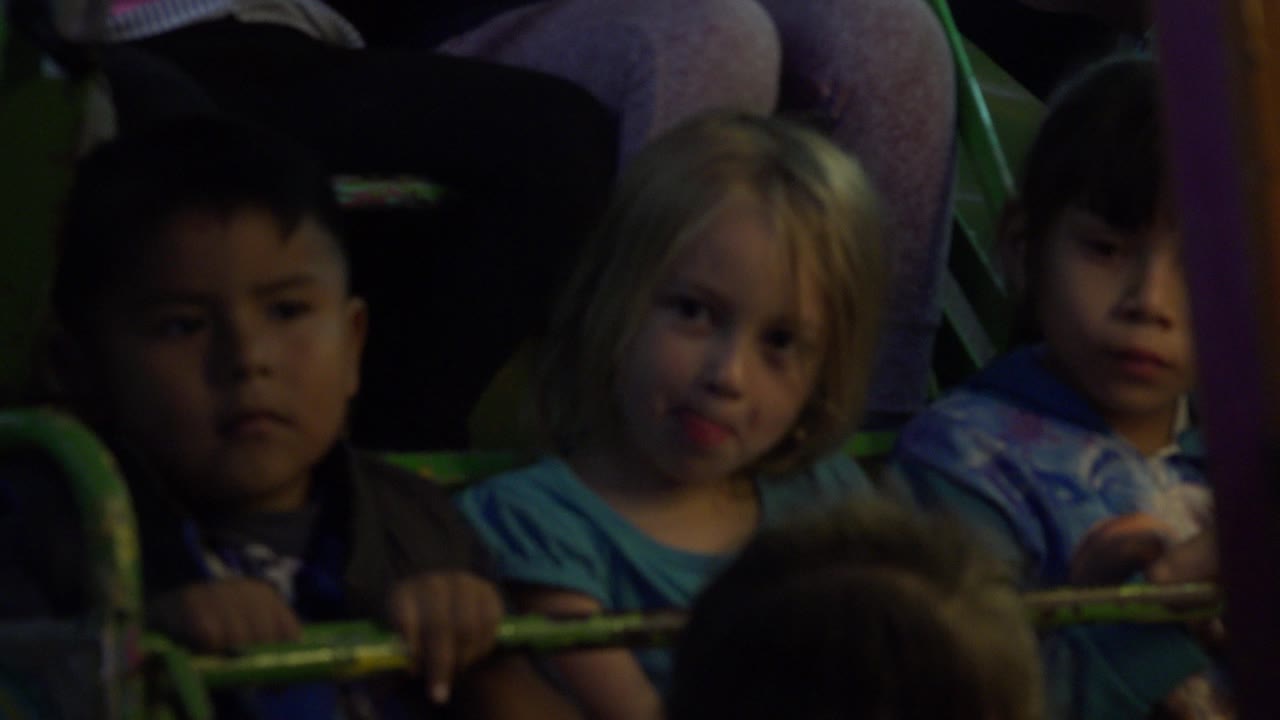 Children seated behind a green ride rail in dim carnival light.