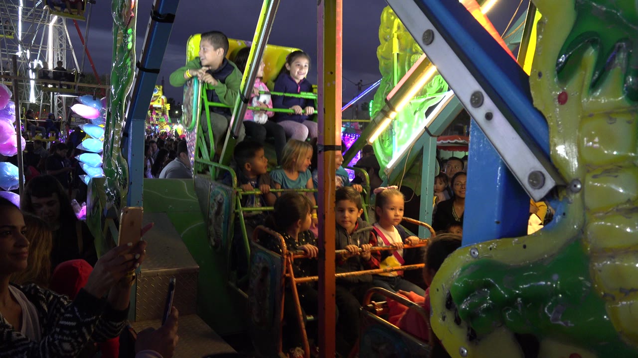 A boy and girl sit high on the amusement ride in San Jose del Cabo, Mexico, while younger children sit below and colored fair lights glow behind them.