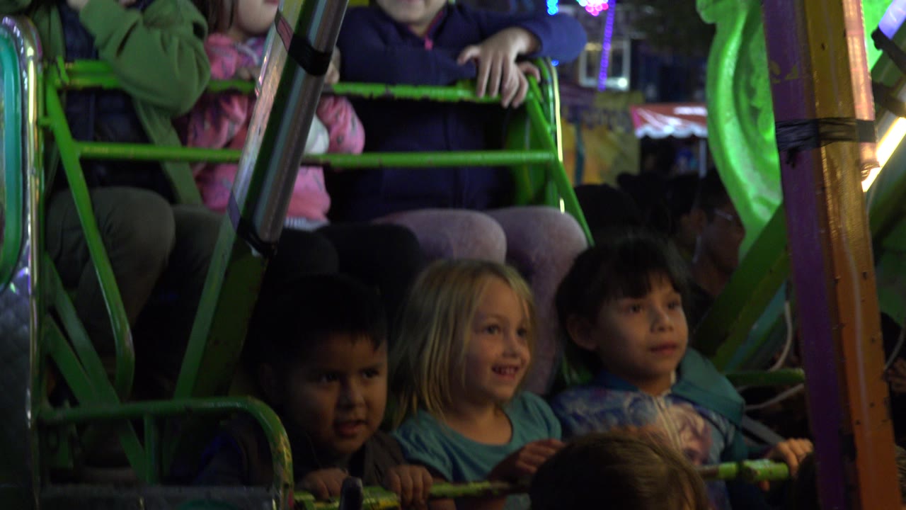 Children seated on a green amusement ride at night