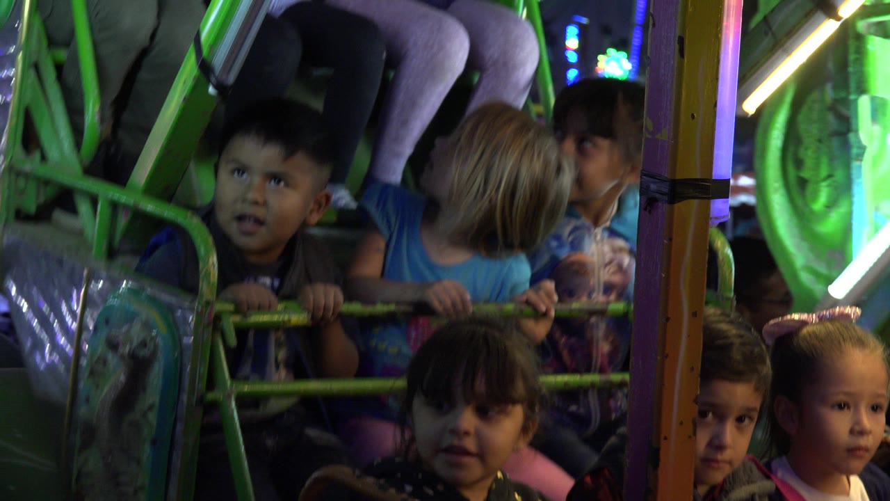 Children seated behind green rails on a carnival ride at night.