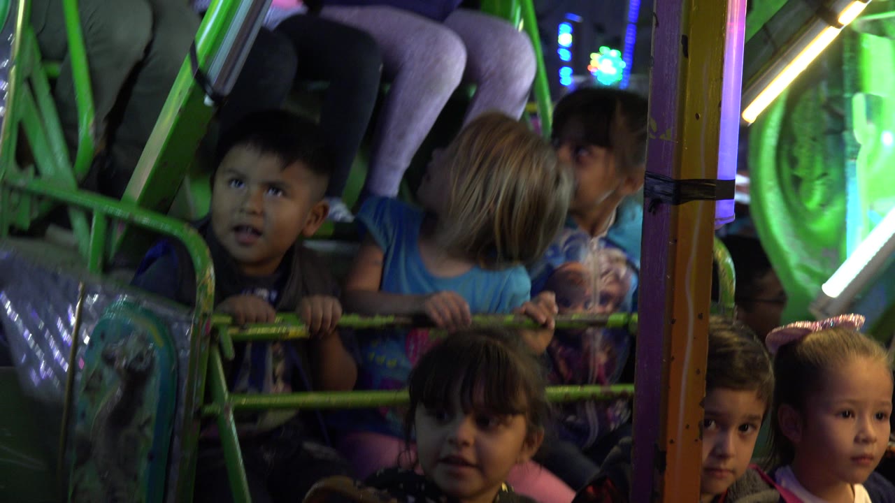 A boy and several girls sit behind the green railing of the pirate ship ride in San Jose del Cabo, Mexico, with white and green light tubes around them.
