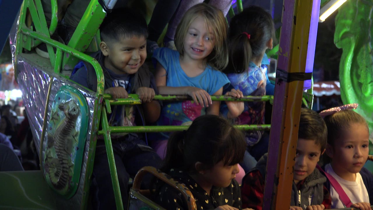 Children riding a green amusement park pirate ship at night.