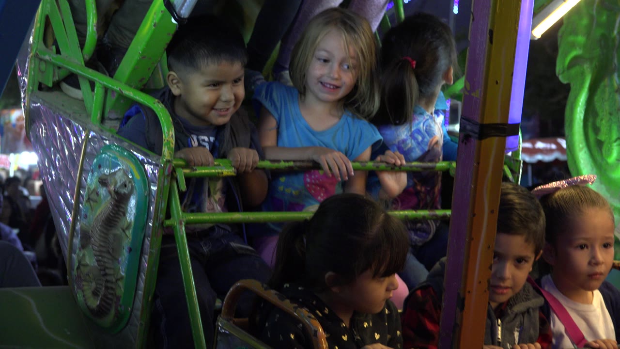 Children remain seated on the green pirate ship ride in San Jose del Cabo, Mexico, with a boy and blonde girl near the top rail and younger children visible in front.