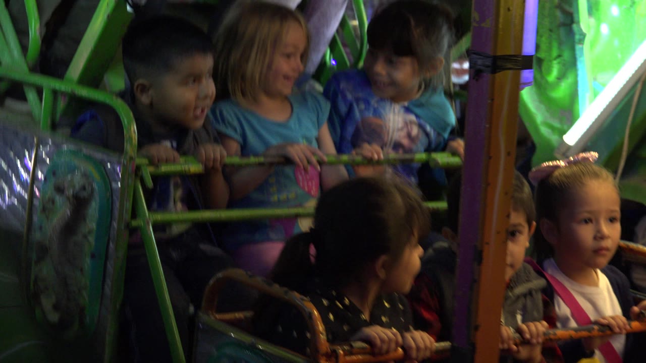 Children riding a green carnival swing ride at night.