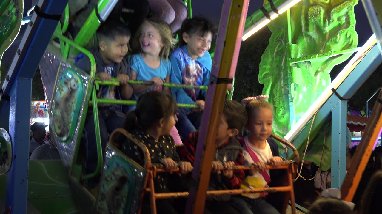 Children seated on a green amusement ride at night.