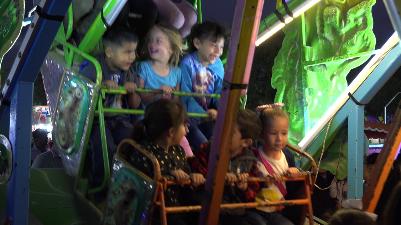 Several children lean toward each other on the green ride in San Jose Del Cabo, Mexico, while a bright green decorative panel and vertical light strip fill the right side of the frame.