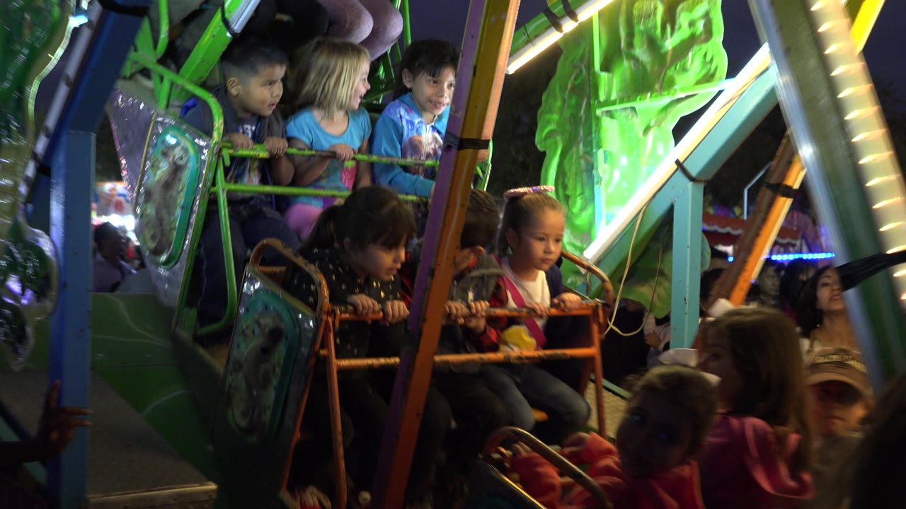 A close view of children in the ride car shows faces, safety bars, and green translucent panels lit by neon strips at the San Jose Del Cabo amusement ride.