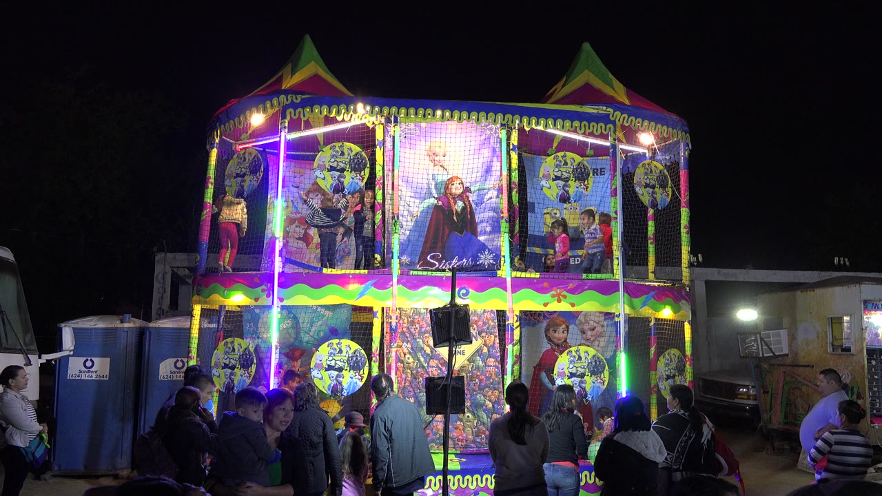 Children play inside a brightly lit inflatable attraction in San Jose Del Cabo, Mexico, while adults stand in the dark foreground at the start of the clip.