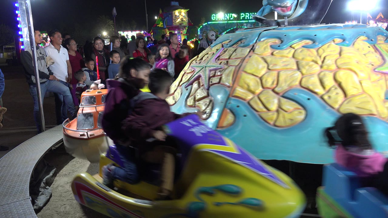 Children ride colorful amusement park cars at night while adults watch nearby.