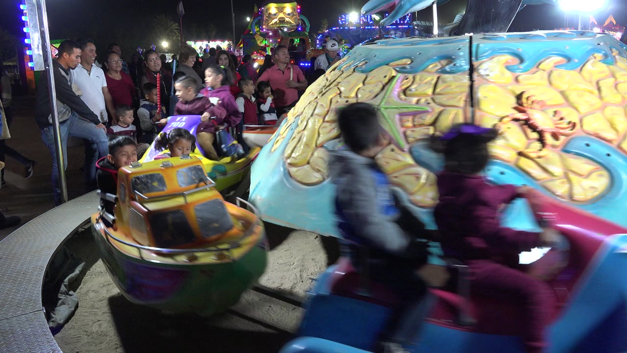 Children ride colorful carousel cars as families watch at night.
