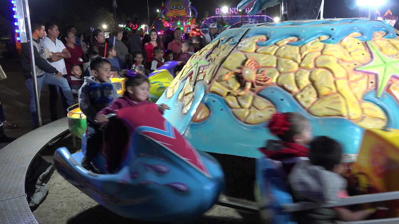Children ride colorful boat and jet ski shaped cars at night.