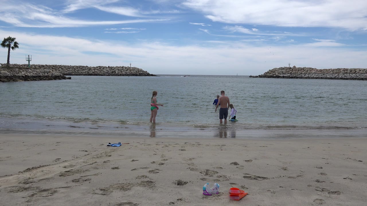 Children and an adult stand at the edge of a sandy beach.