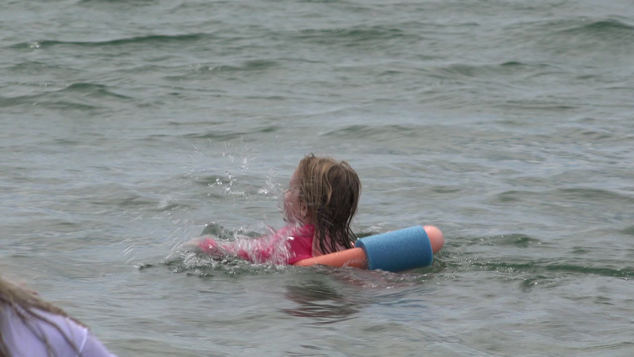 Young girl paddling in the ocean with a pool float.