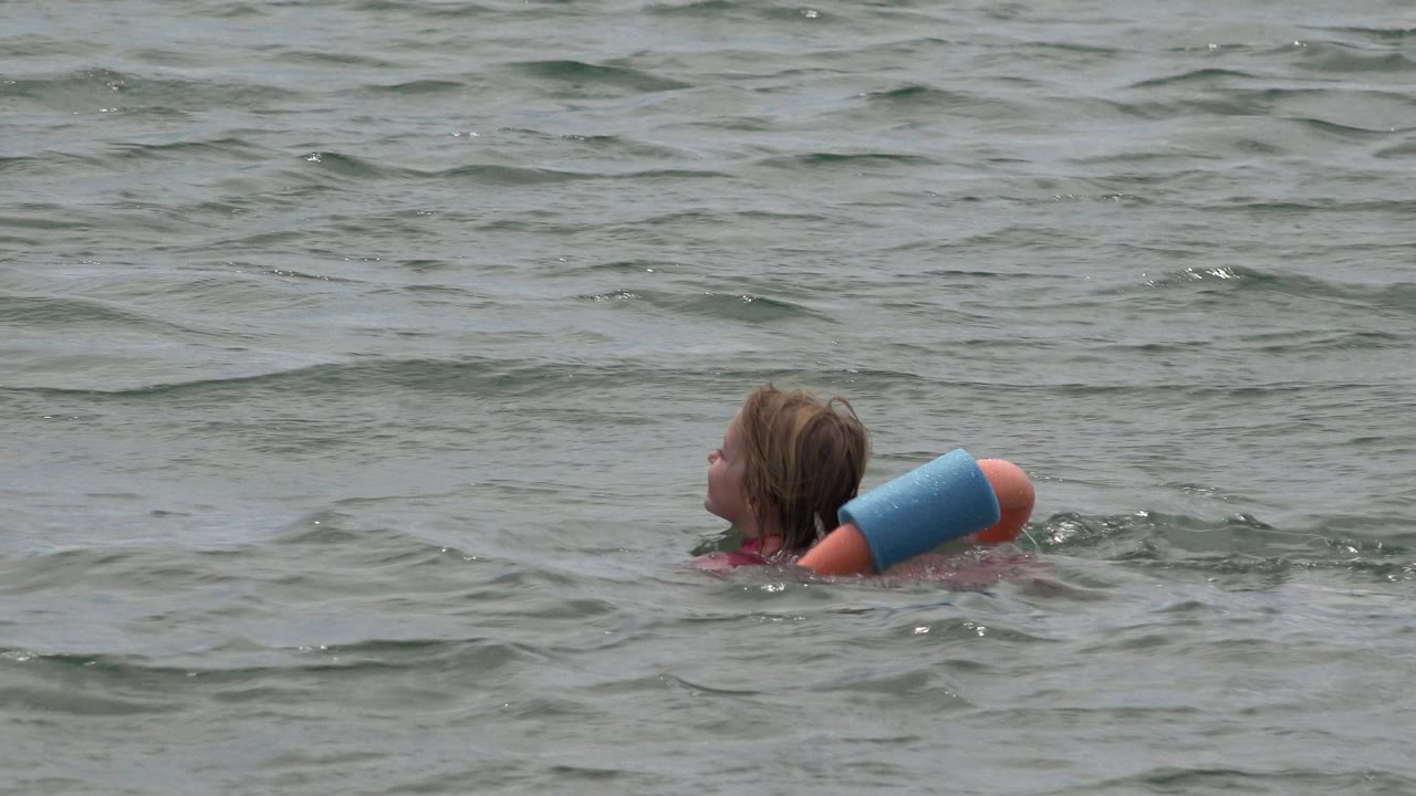 The girl continues floating in San Jose del Cabo water, with the swim ring angled across her back and ripples rising around her shoulders.