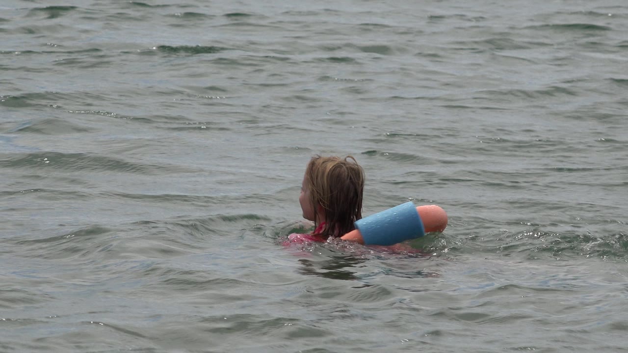 Girl seen from behind floating farther right in open water.