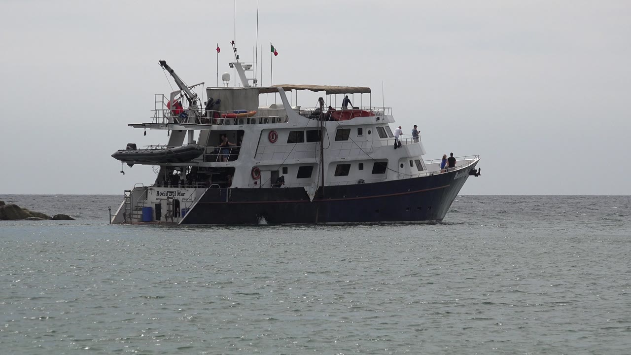 Passenger boat beside low rocks on gray water.