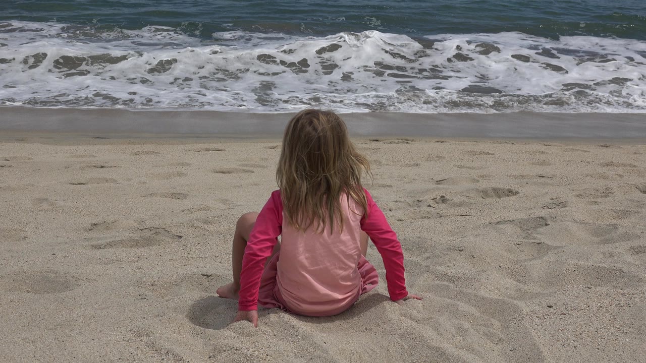 The child remains seated with both hands in the sand as a thin line of surf stretches across the San Jose del Cabo beach background.
