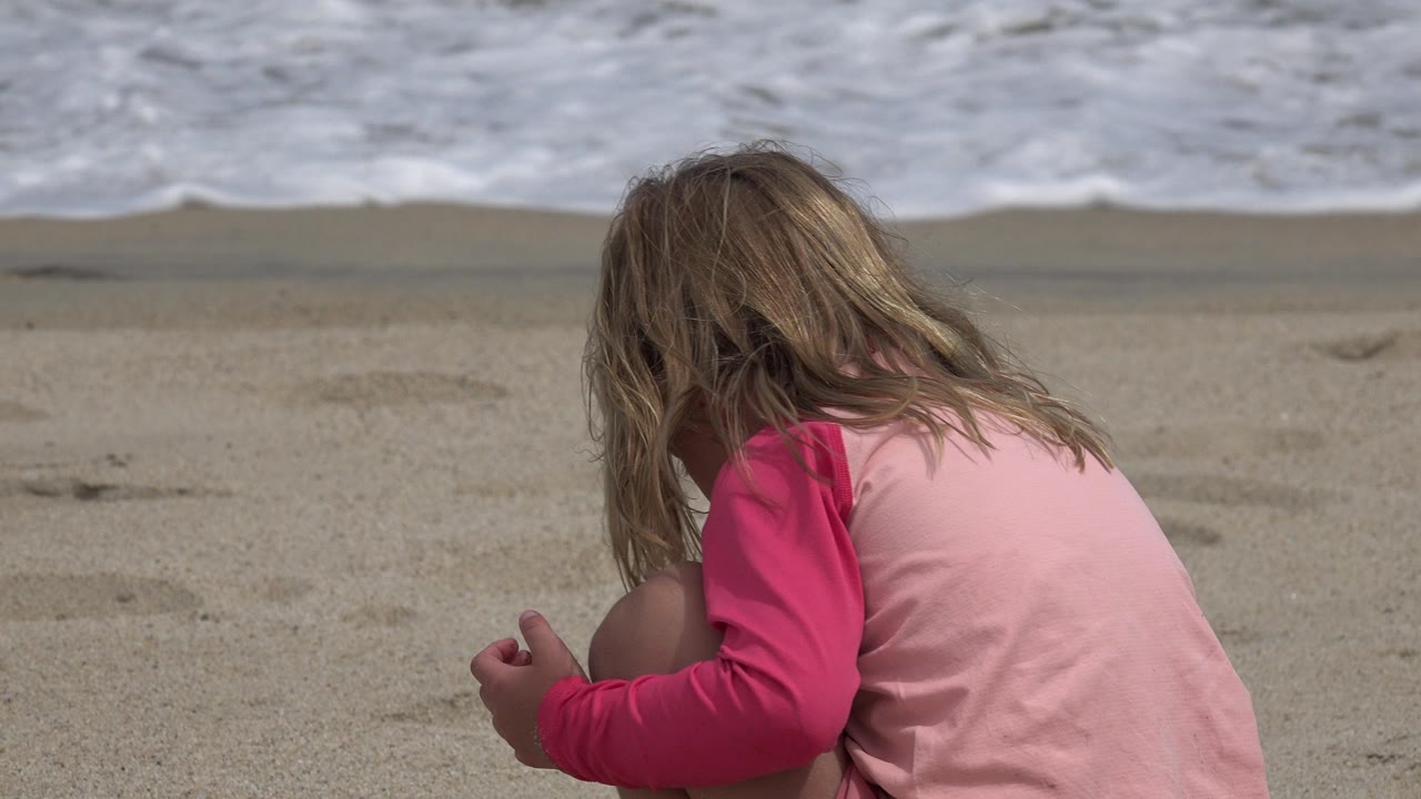 The child remains seated low on the San Jose del Cabo beach, turned away from camera as waves foam along the top of the frame.