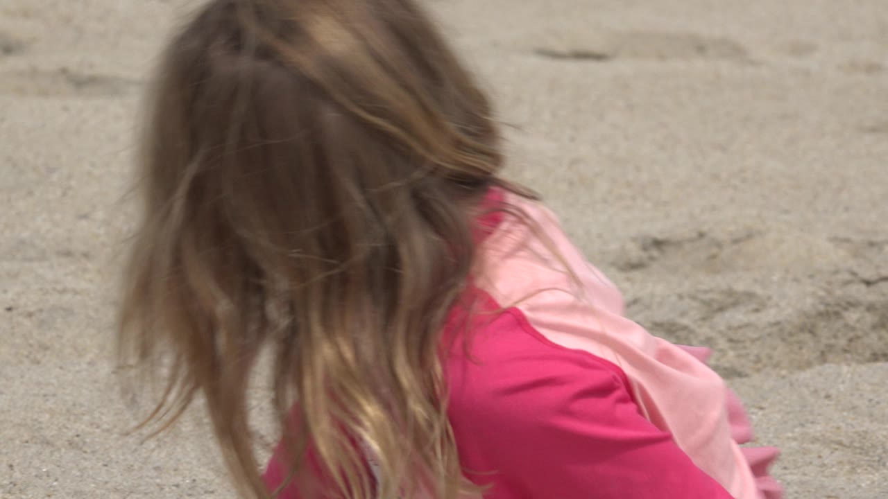 Girl turning away while seated on sand.