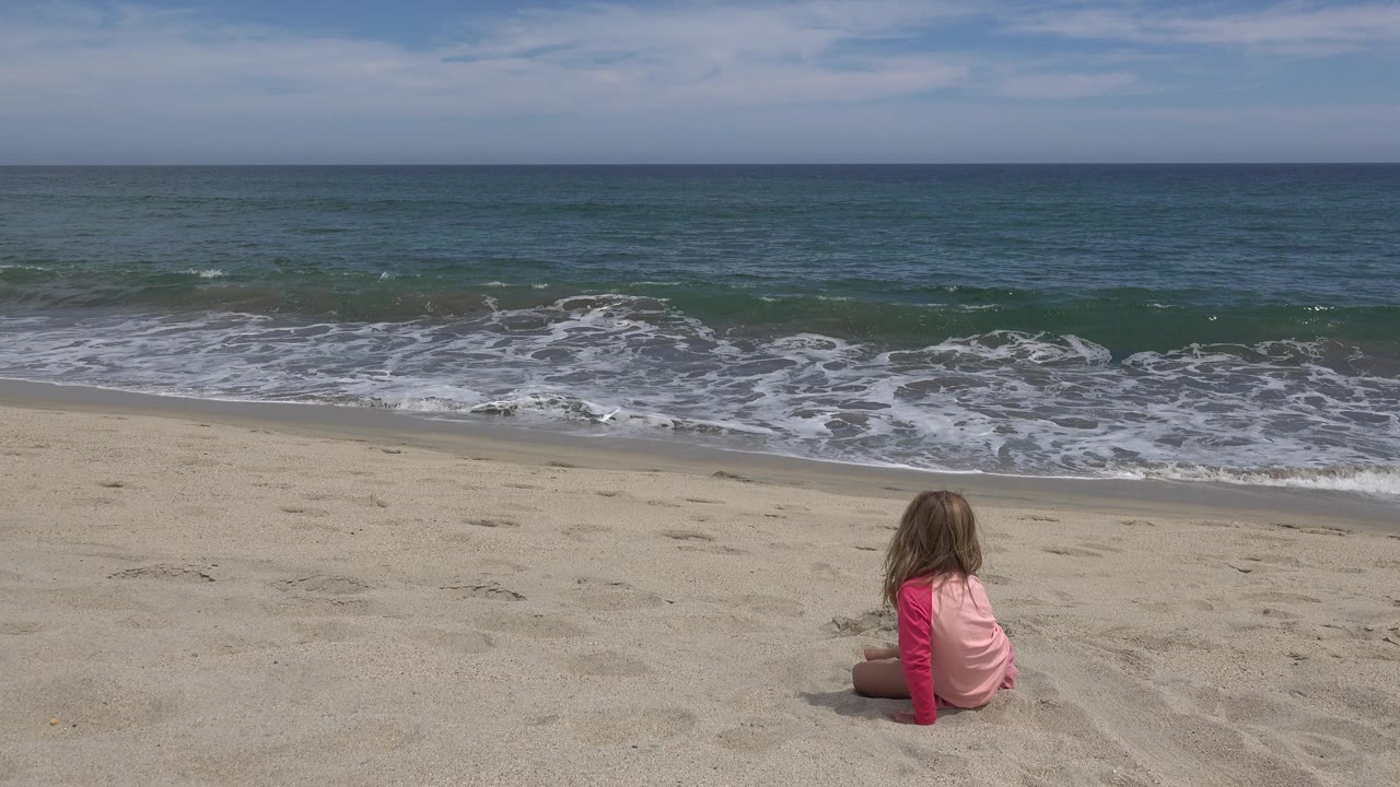Child on beach with breaking surf behind.