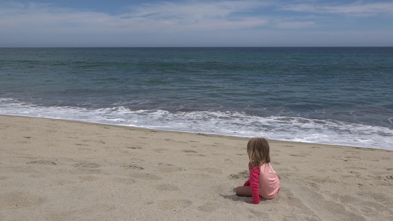Young girl sitting near the lower right of a wide beach view.