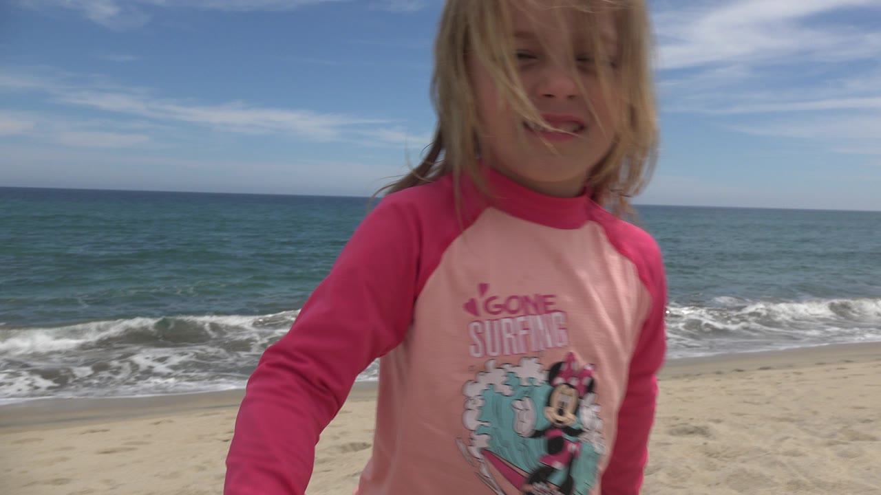 Young girl in a pink rash guard standing near the ocean.
