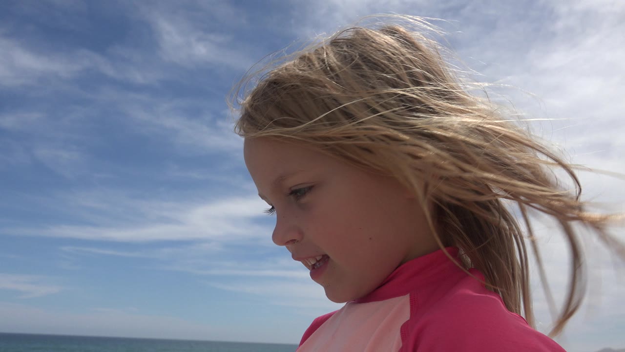 Young girl in a pink top beside the ocean under a blue sky.