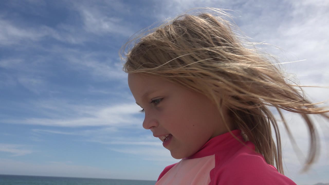 The child remains in a tight side view in San Jose del Cabo, her hair blown across the frame while the ocean horizon sits low behind her.