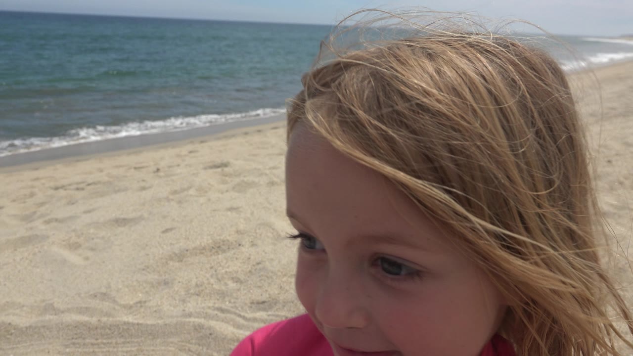 Young girl close to camera on a sandy beach with ocean waves behind her.