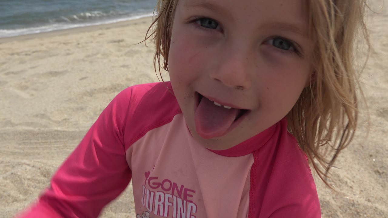 Young blonde girl close to the camera on a sandy beach.