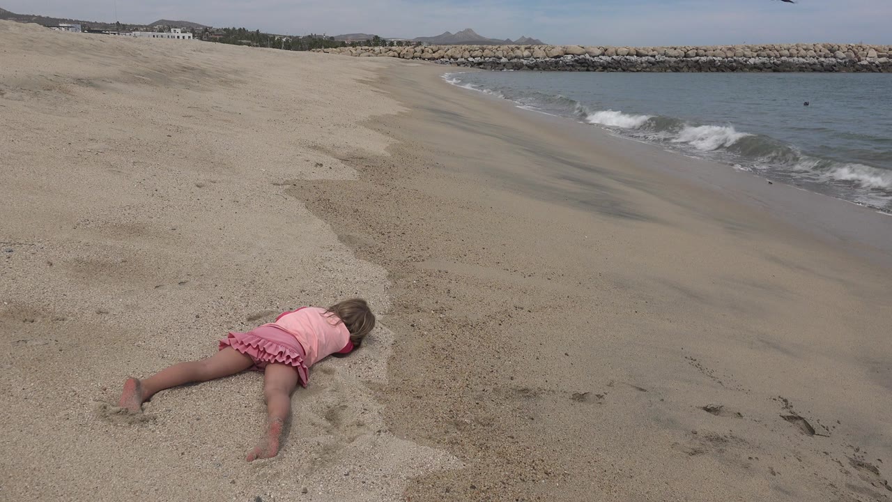 Young girl lying on sand near a small wave at the beach.