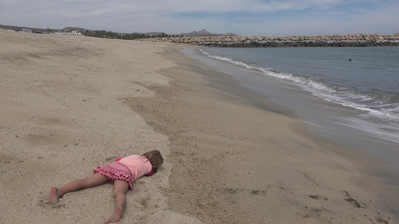 Girl on sand with waves rolling behind her.