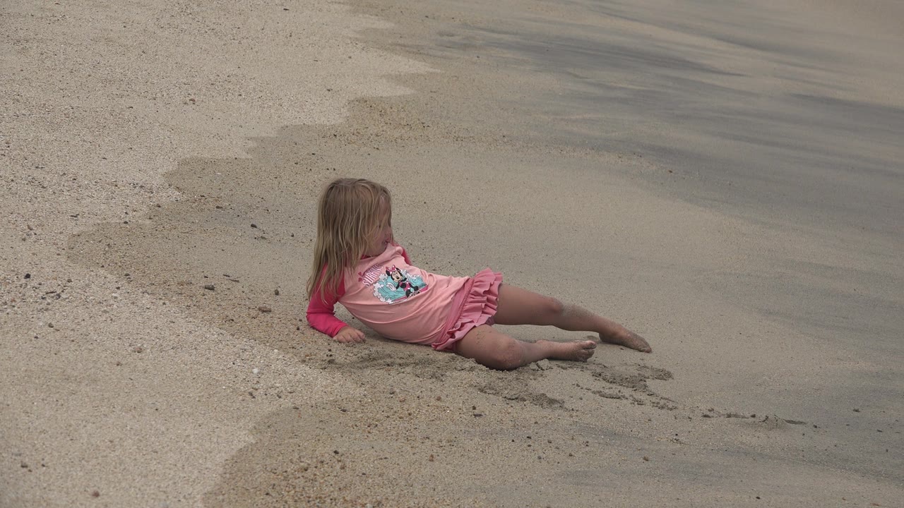 Girl seated on sand with wet beach stretching behind her.