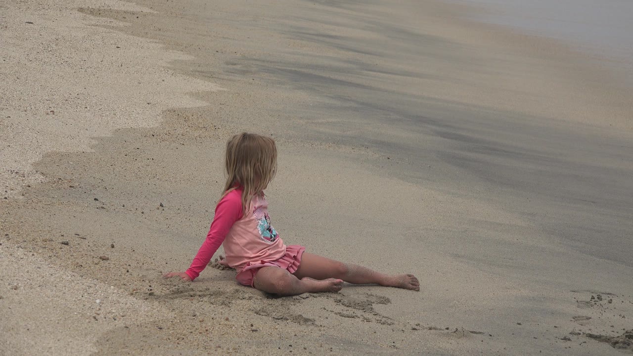Young girl sitting on sand near shallow surf.