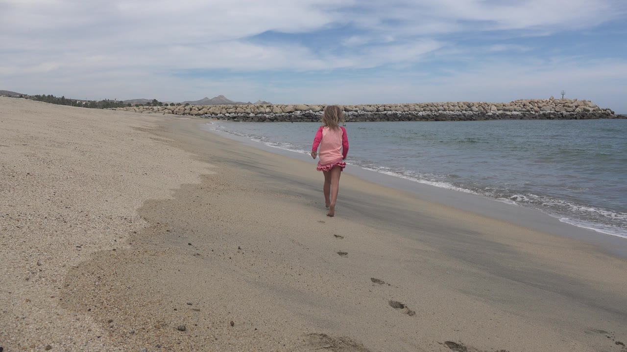 Young girl in pink on a sandy beach near the shoreline.